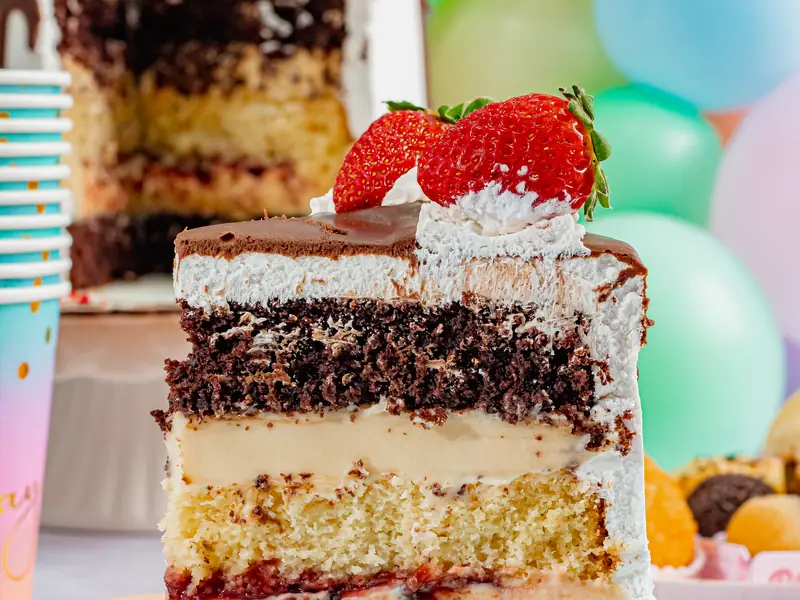 Fatia de torta com camadas de massa de chocolate e massa branca, recheio e morango no topo