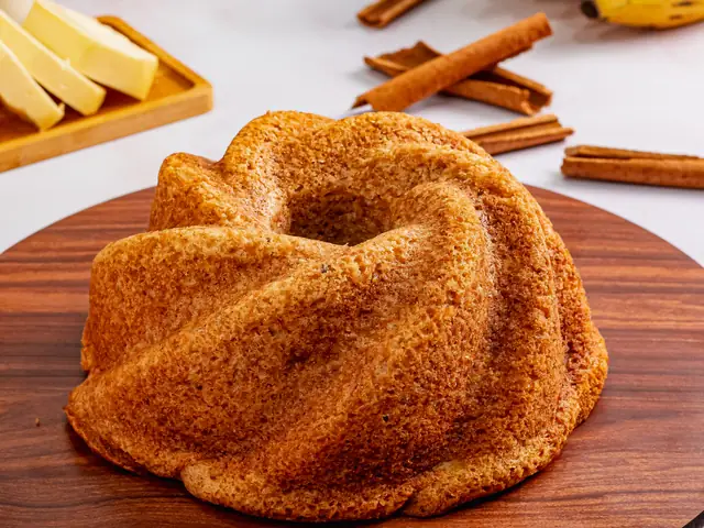 Bolo de banana em forma de anel com canela e bananas ao fundo