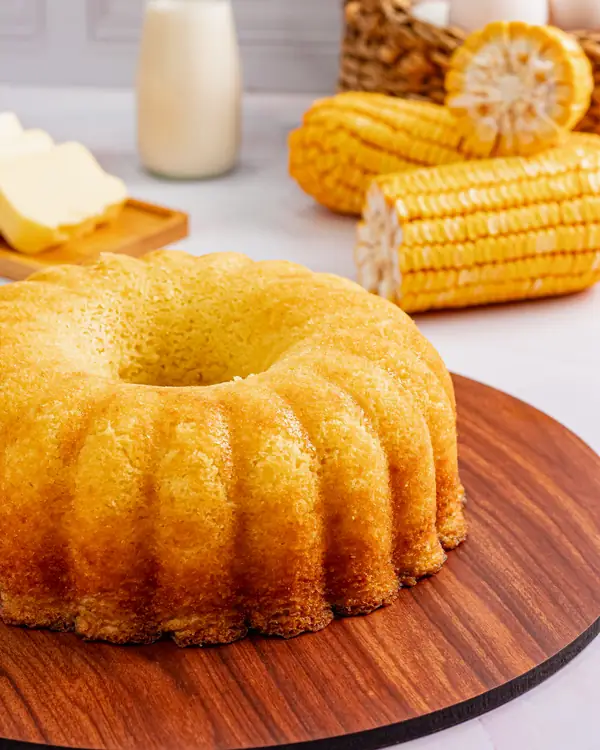 Bolo de milho em forma de anel, com espigas de milho ao fundo