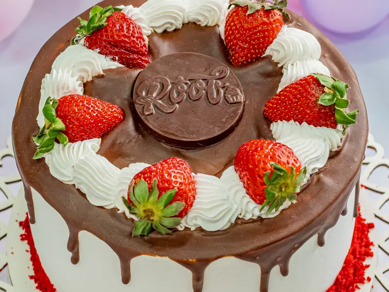 Torta decorada com chantilly, calda de chocolate escorrendo e morangos frescos no topo